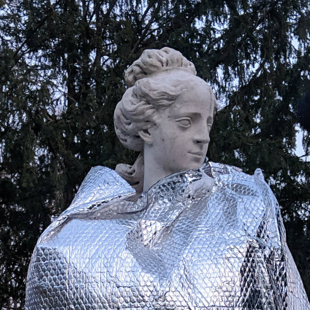 A statue of a woman covered up to the neck with a foil blanket.