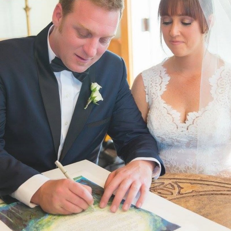 You can see how much this couple's love is glowing! Which is the perfect caption because that's what their ketubah is called! The groom is signing the Glowing Love Ketubah that has been a top seller for years.