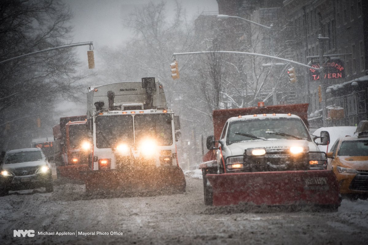 Sanitation trucks and snow plows make their way through the snow.