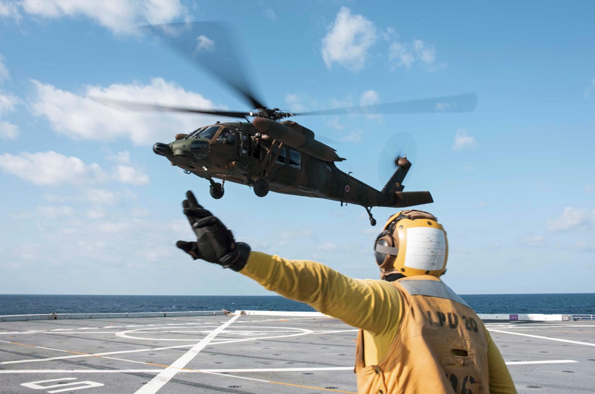 .@USNavy Petty Officer 3rd Class Dion Sanders signals to a UH-60 Black Hawk helicopter on the flight deck of #USSGreenBay in the Philippine Sea.