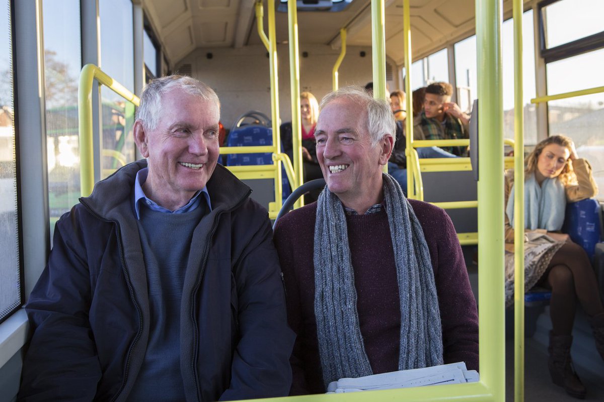 Two older men smile as they ride on a bus