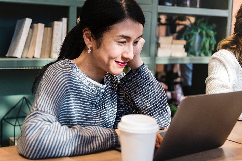 woman smiling looking at her laptop with a coffee next to her