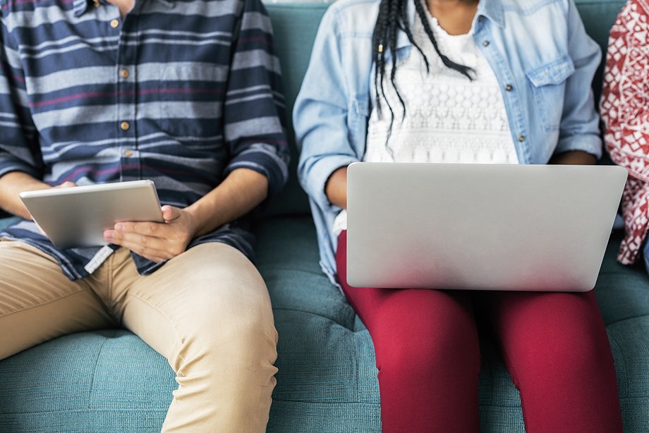 two people sitting next to each other on their laptop and tablet.