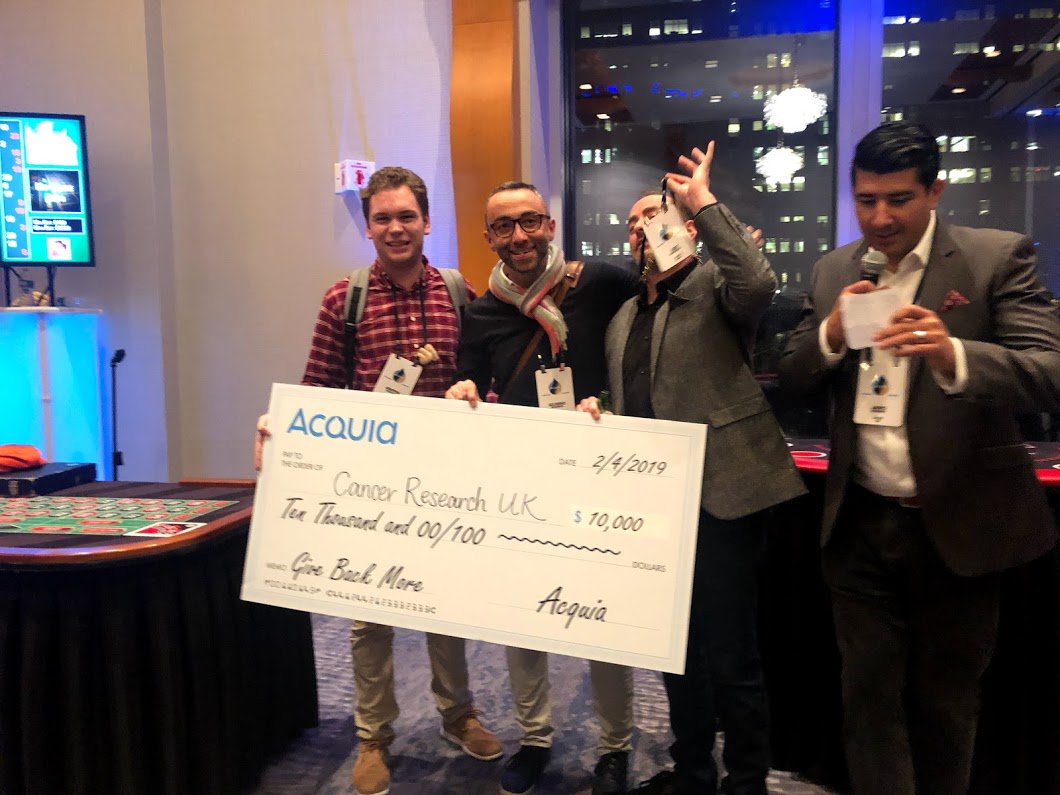 acquia's tweet photo. Acquia Sales &amp; Marketing #Kickoff day 1 in the books. It was great to gather with our international marketing &amp; sales teams. Casino night wasn't bad either - we're donating $10,000 to @CR_UK! #strongertogether #AcquiaKickoff #SMKO #giantcheck! #casinonight #theoffice #SMKO2019 https://t.co/9DJjXld3BI