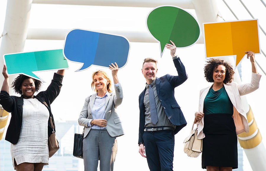four people standing with different text bubble paper cut outs above their heads and they are smiling