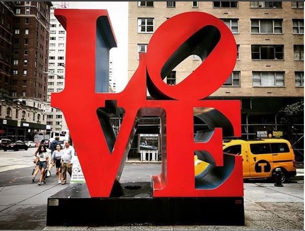 The image shows the LOVE statue in New York City, with a yellow taxi in the background.
