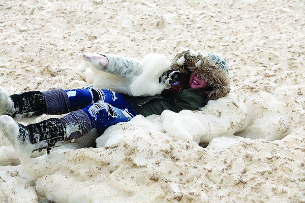 Laura Godoy clowns around in sea foam as it billows up along East Cliff Drive at Twin Lakes Sate Beach Thursday morning.