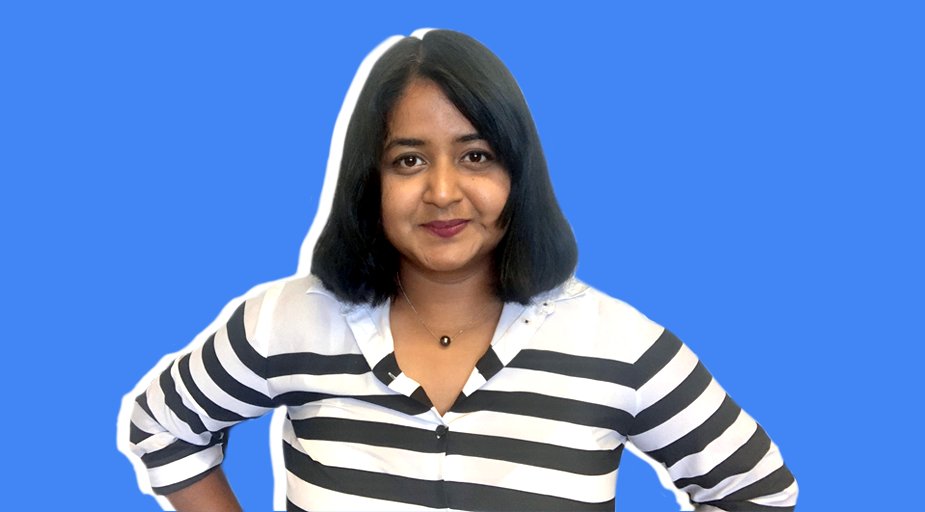 A head shot of Debbie Biswas, looking straight at the camera with a closed-mouth smile. She's wearing a white collared shirt with black horizontal stripes, and she appears to have her hands on her hips.