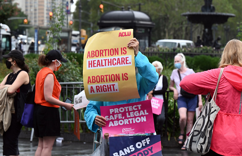 Person holds signs saying "Abortion is Healthcare. Abortion is a Right." and "Protect Safe, Legal Abortion"