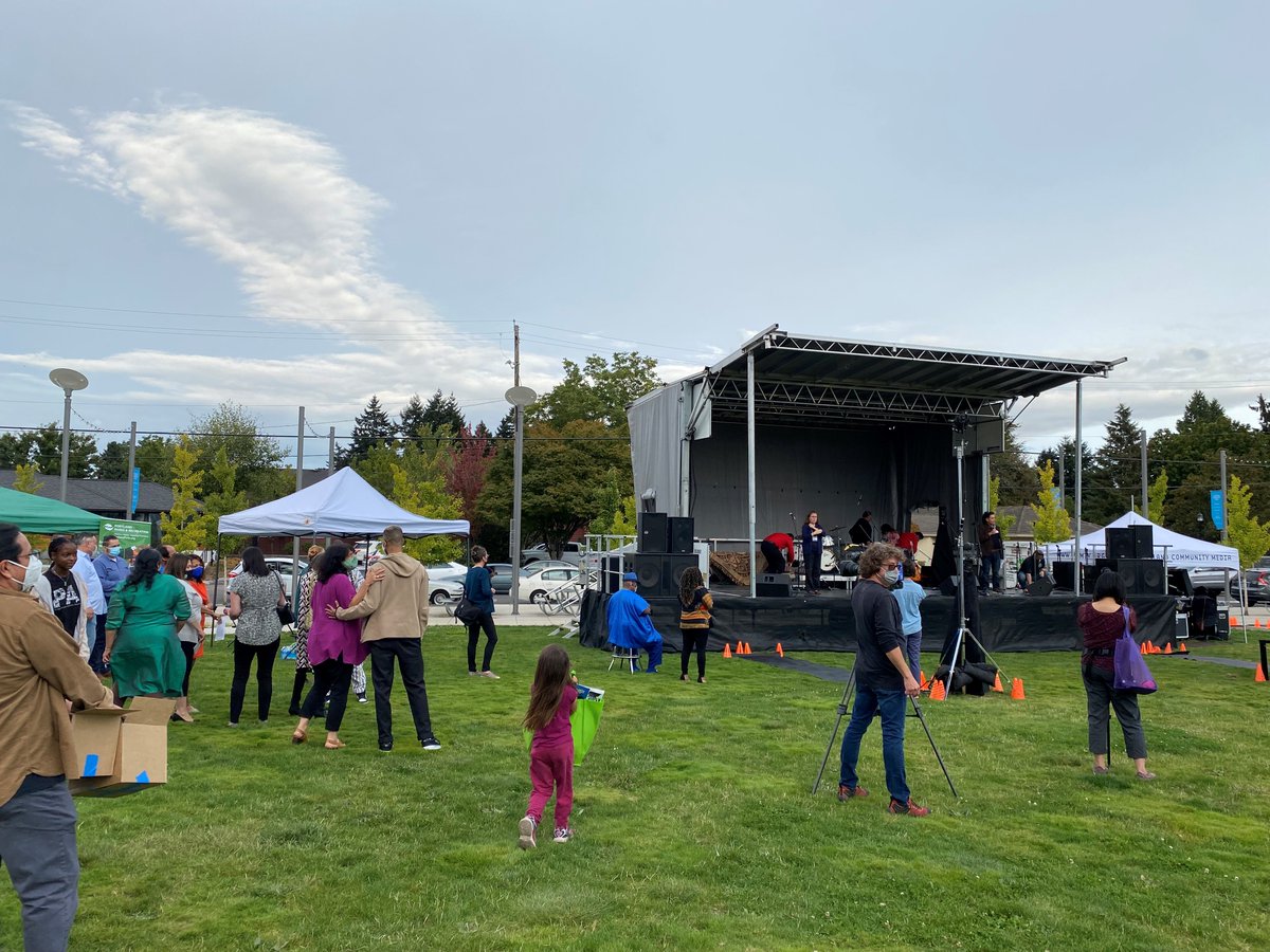 Photo of a grassy field, portable stage, pop up tents and people milling about.