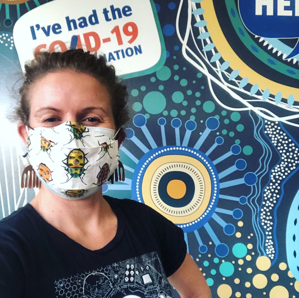 A lady in a facemask infront of a COVID vaccination sign