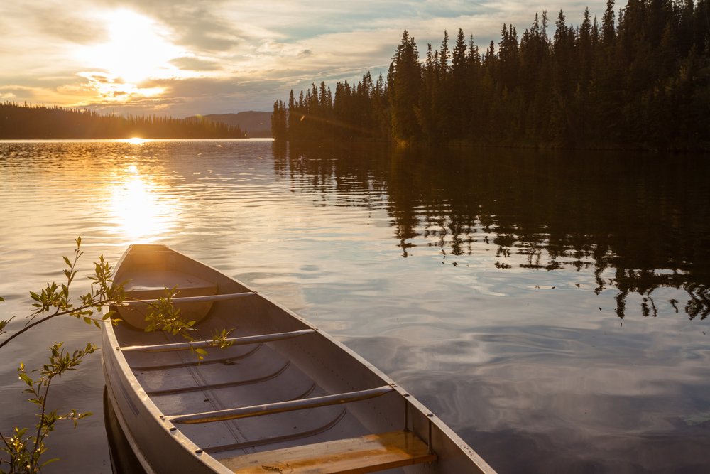A canoe tied to the shore and facing an early sunset in Frenchman Lake, Yukon Territory. 