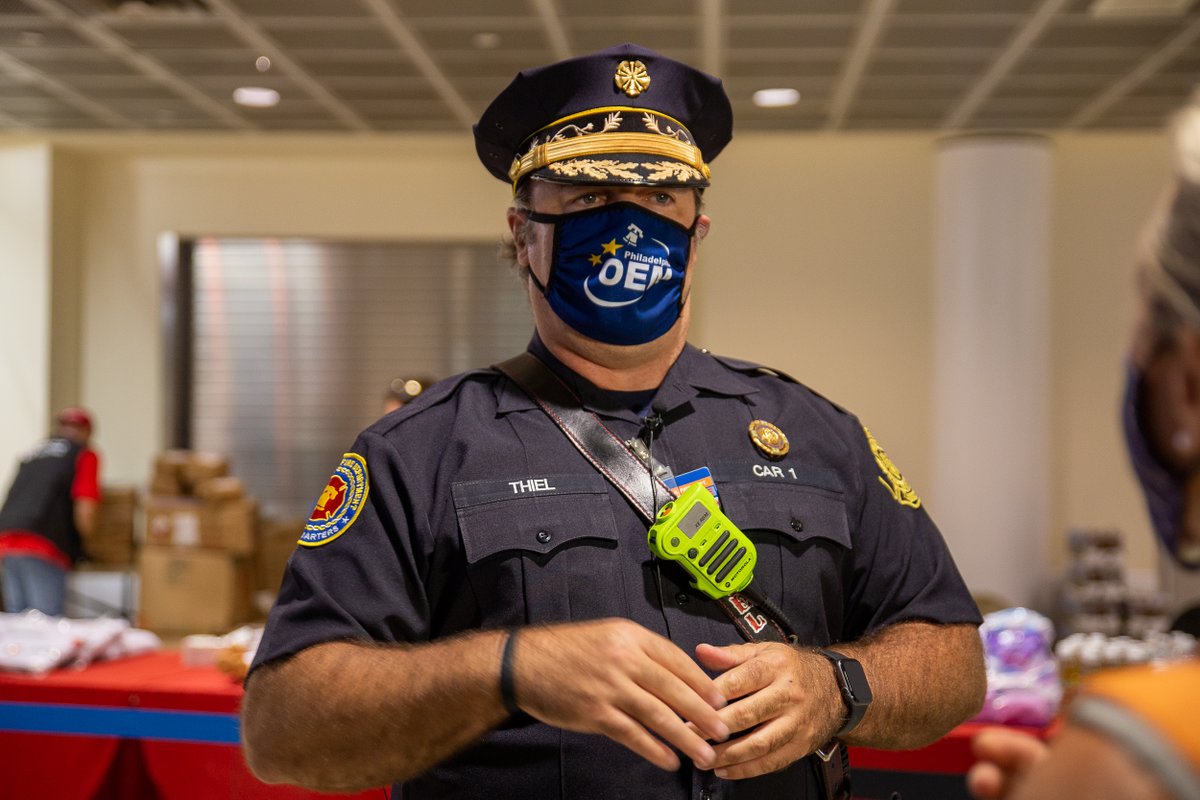 man in uniform with dress cap and wearing radio across his chest and face mask that says OEM