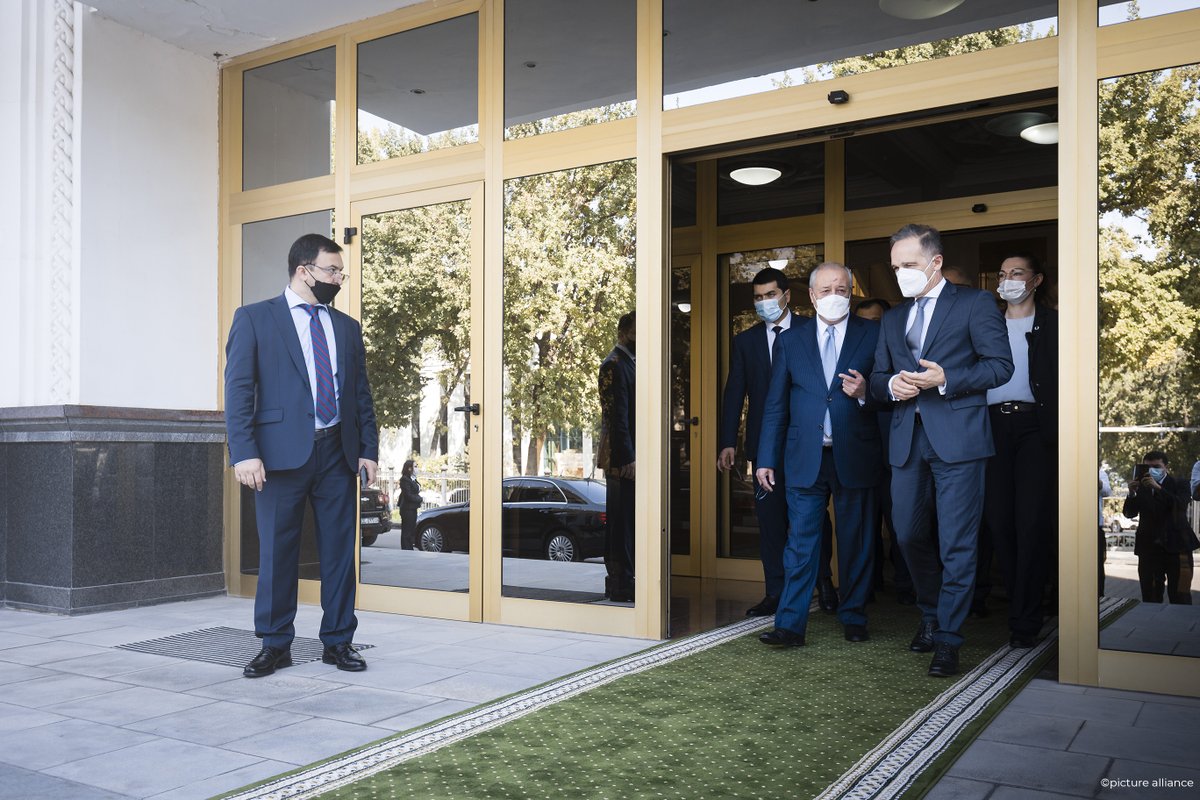 German foreign minister exits a meeting with Uzbekistan's foreign minister on Monday. They walk along a green carpet, and are trailed by masked people. The doors/windows of the building are plated gold.