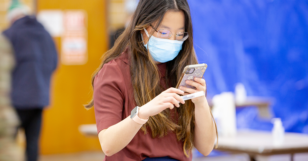young adult scanning COVID-19 saliva test tube at community test site.