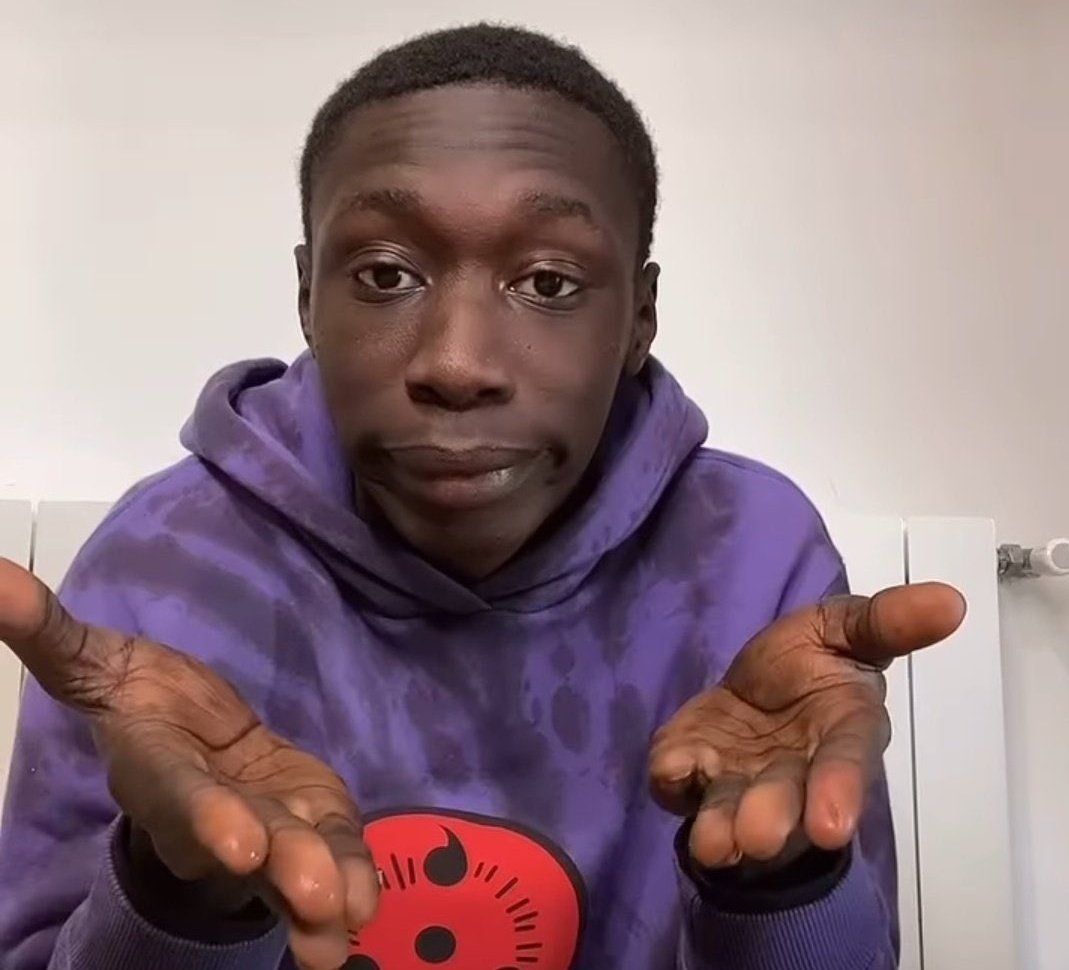 Photo of Tiktok star Khaby Lame wearing a purple hoodie with sharingan insignia doing his signature facial expression with palms up to indicate that this task is very simple. 