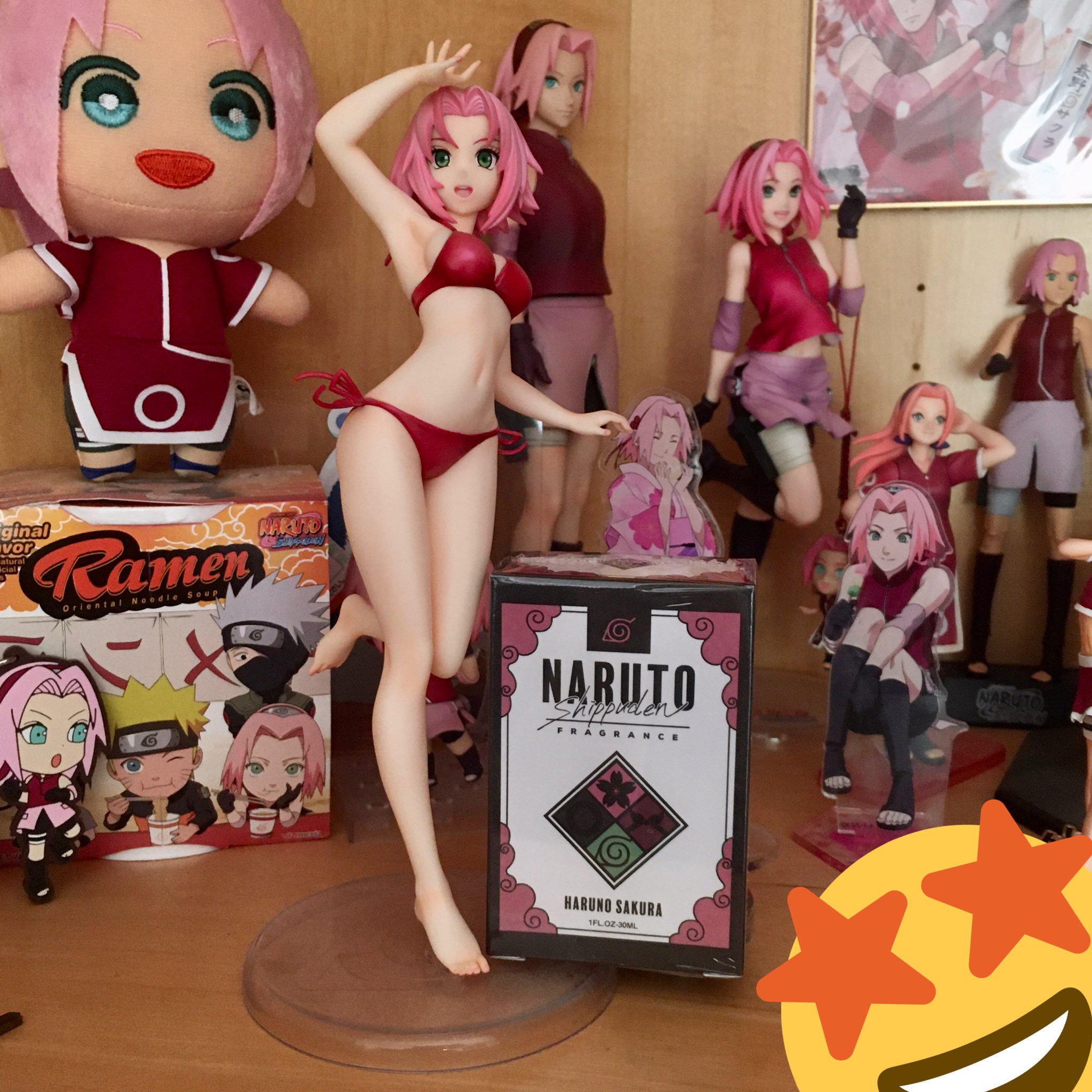 Photo of a shelf displaying multiple figures and goods featuring Sakura Haruno from Naruto. In the front is an unopened box of Sakura Haruno Perfume from primaniacs, a Japanese perfume company.