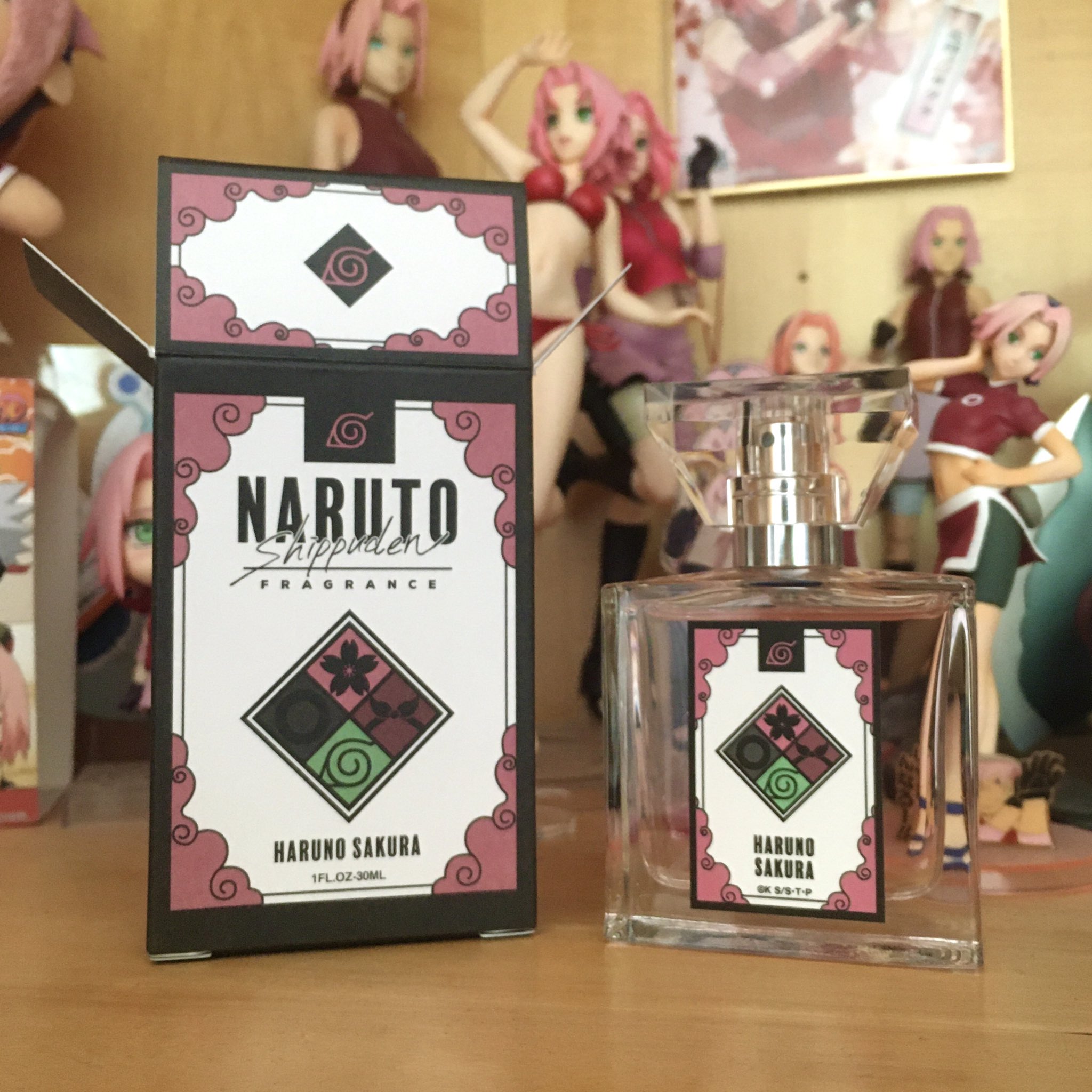 ImagePhoto of a shelf displaying multiple figures and goods featuring Sakura Haruno from Naruto. In the front is an opened box of Sakura Haruno Perfume from primaniacs, a Japanese perfume company, with the perfume bottle out beside it.