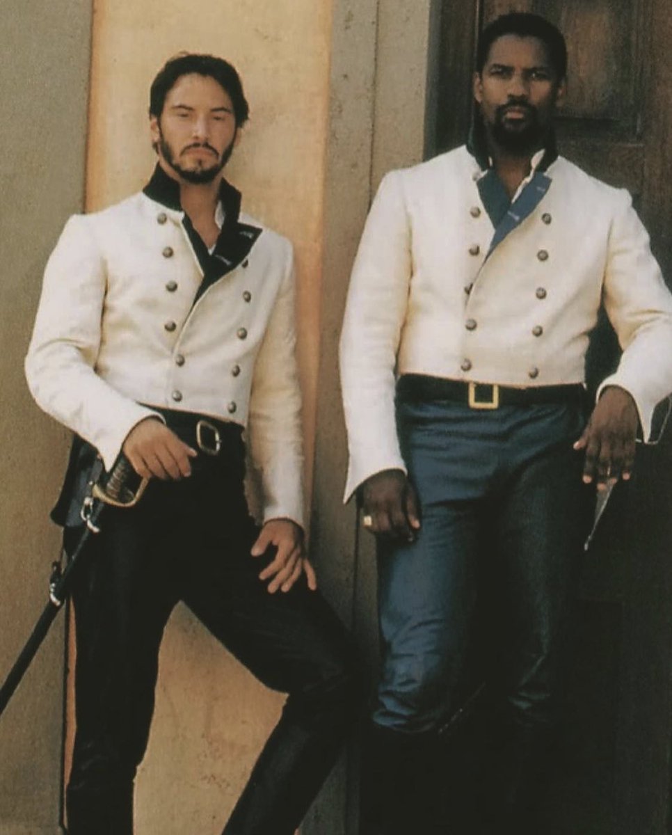Denzel Washington and Keanu Reeves from Much Ado About Nothing looking FINE in blue uniform pants, swords, and white doublets with double rows of brass buttons. Leaning jauntily against a door.