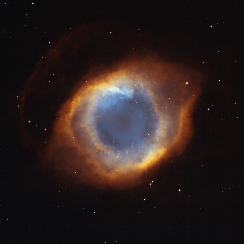 The Helix Nebula resembles an eye. In this Hubble image, the "pupil" is a blue-gray circle at the center. Surrounding the blue-gray circle are red-orange edges that form an overall almond shape.