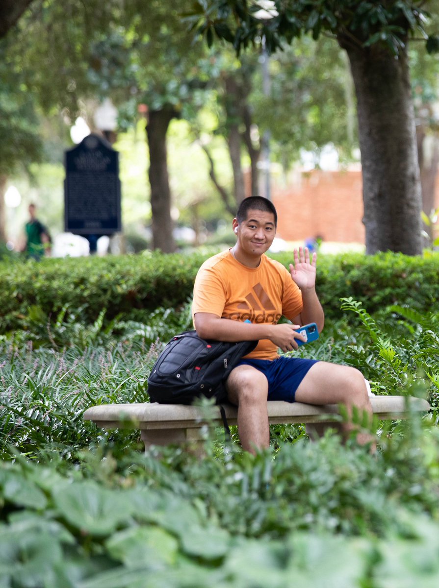 A student smiles and waves in an orange shirt