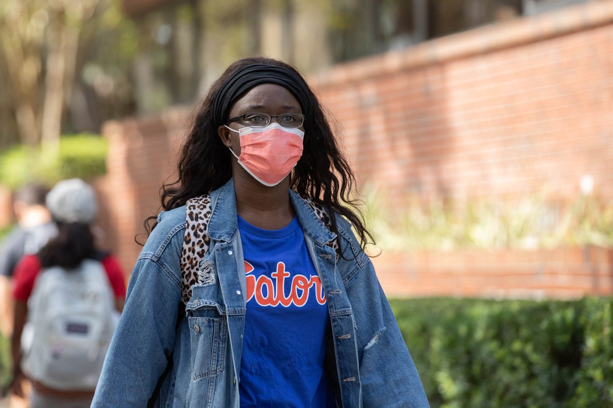 A student walks to class in a blue shirt and orange mask