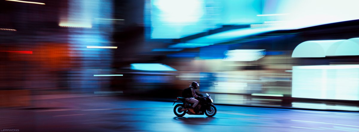 Photography by Liam Wong of London at night. A man on a motorcycle zooming through an empty Piccadilly Circus at 4am. He's the only visible thing in the frame. The background is motion blurred from a rolling shot technique.