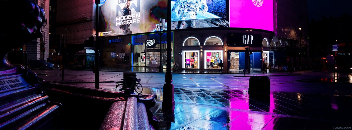 Photography by Liam Wong of London at night. An empty Piccadilly Circus at 4am in the rain. The billboards reflect on to the pavement in pinks and blues. One billboard has Call of Duty, another has an astronaut.