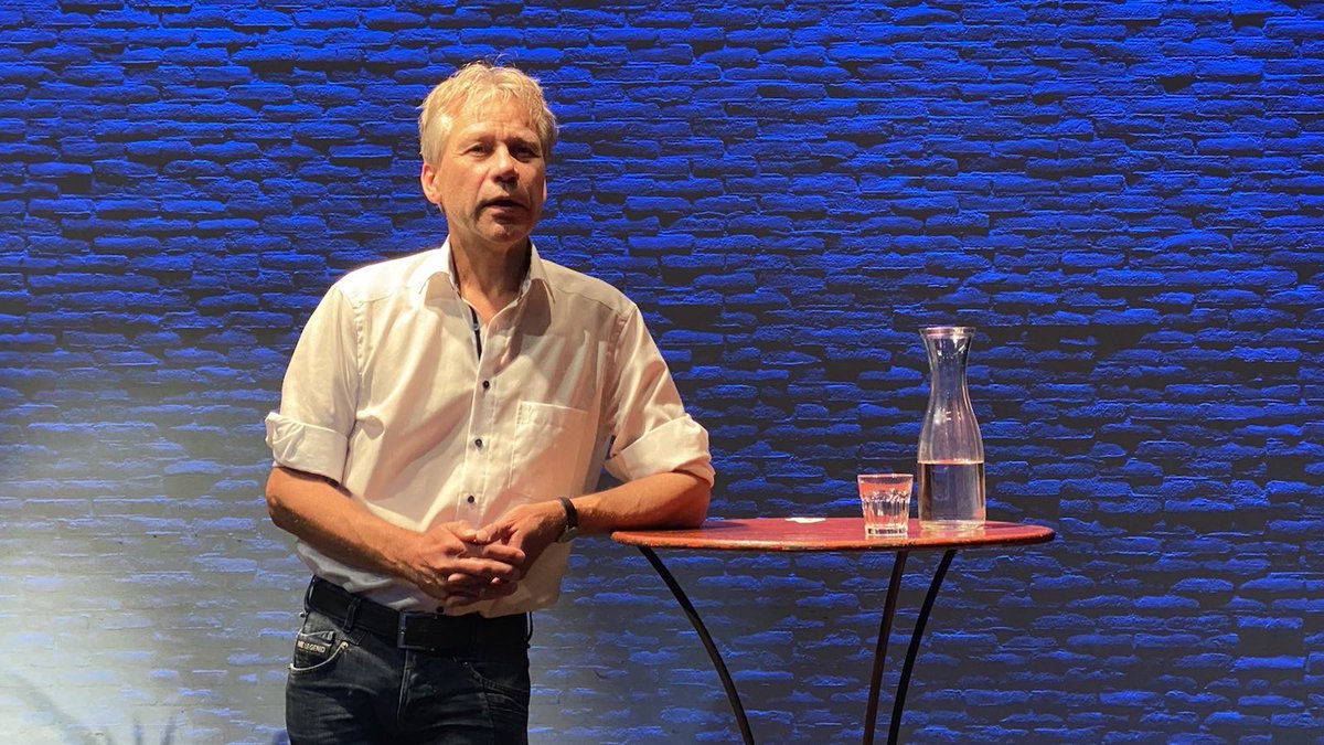 Een foto van Rik voor een blauw-verlichte muur, leunend op een statafel.