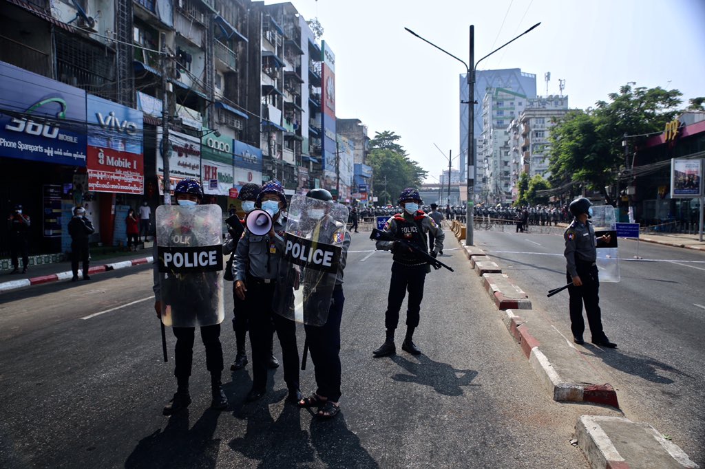 ANachemson's tweet photo. Been going through some old photos. Hard to believe this was seven months ago. Feb 6, 2021, the first mass protest against the coup in Yangon. Protesters confronted by police as bystanders wave on in support from a nearby rooftop https://t.co/zBqSKrfZjO