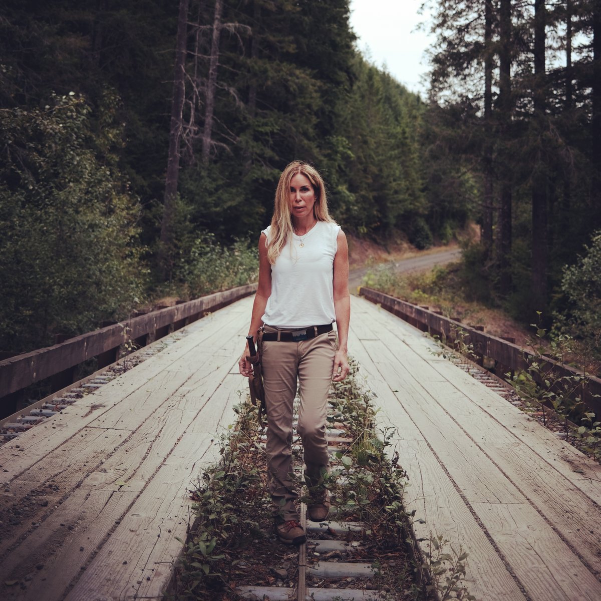 Mireya Mayor in khakis and boots, walking across overgrown railroad tracks ...