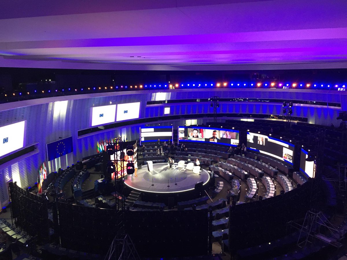The plenary chamber of the European Parliament in Strasbourg are visible in the photo. Armchairs and a podium are present on a stage set at the centre of the hemicycle. Technical checks are underway.