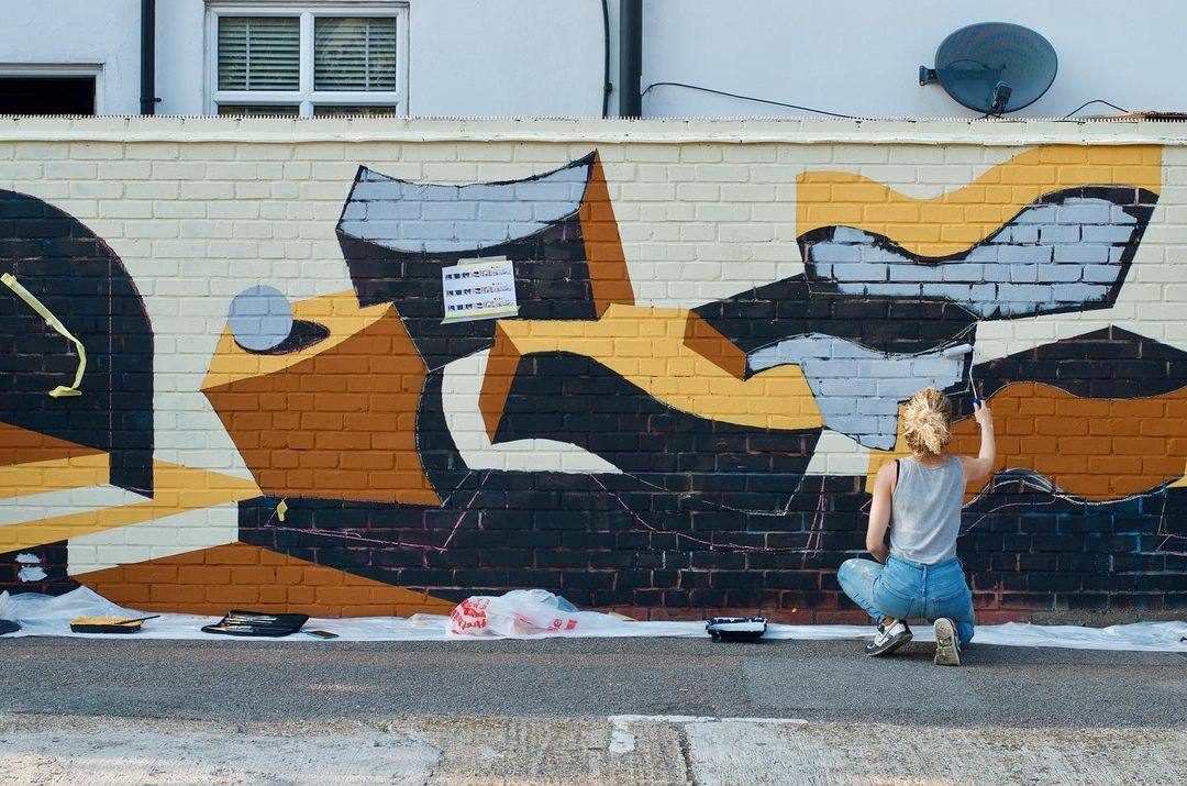 Adriana Jaros working on an outdoor brick wall mural.