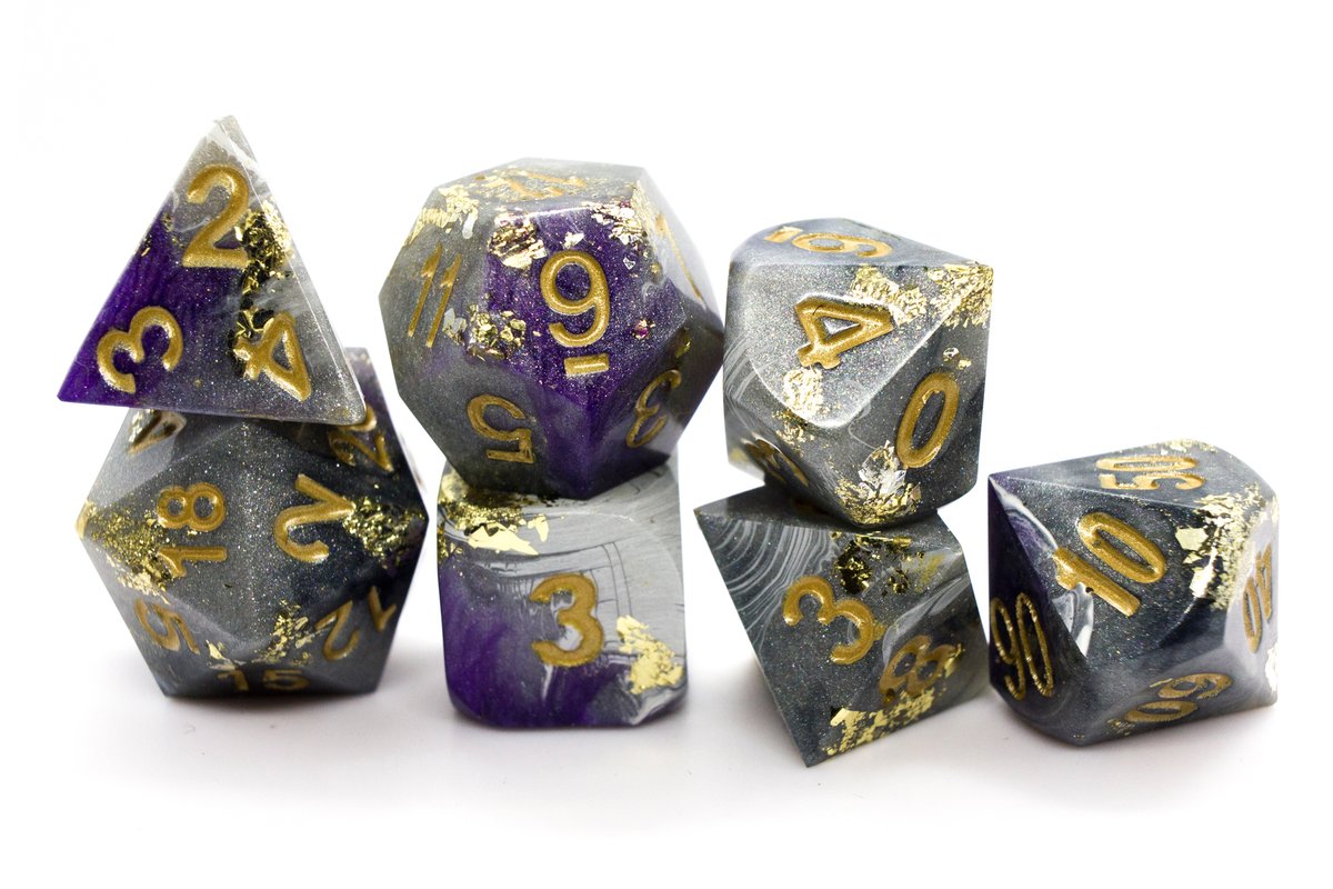 Handmade resin dice in different shades of grey and white with purple swirls, gold leaf foil and gold ink for the numbers, very minor flaws on some of the facets that face the lid --> 70 Euro excluding shipping.