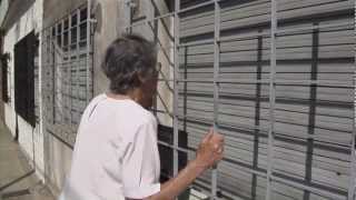 En esta imagen Milka González conversa con una persona detrás de una persiana que no se levanta. Esa era la casa de su hijo, hoy apropiada, cuando lo raptaron en Buenos Aires en un operativo militar. 
Acá la película completa:
vimeo.com/552843738