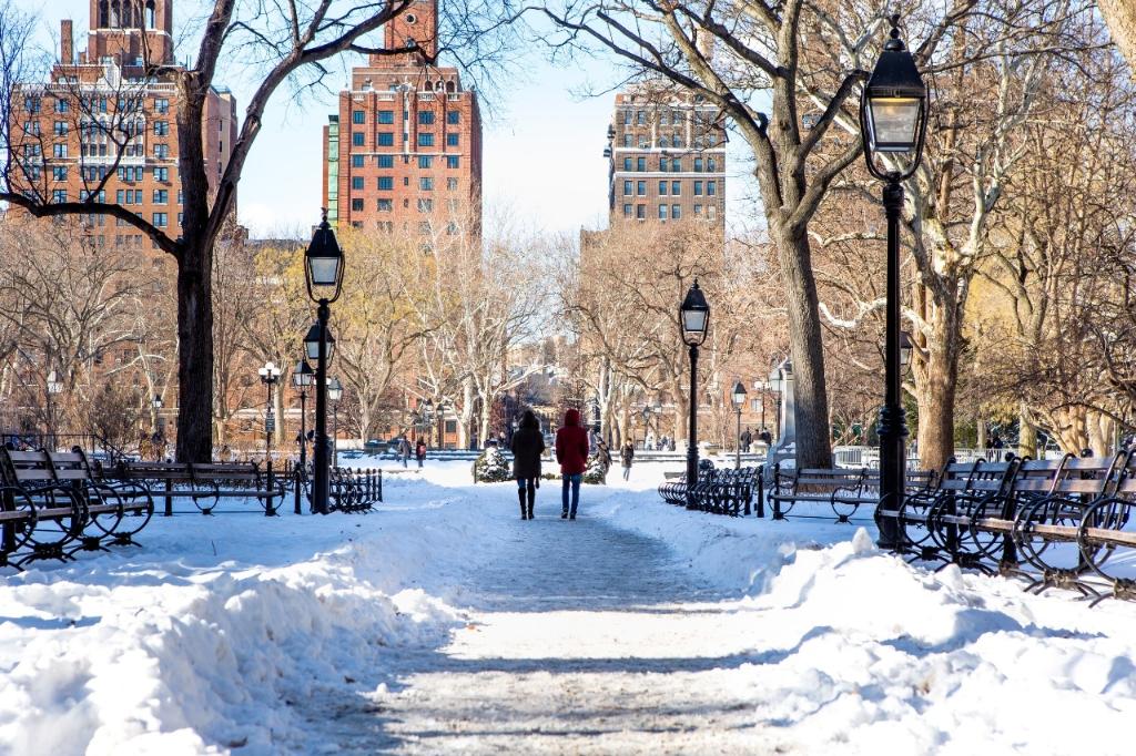 Two students walking through a snowy Washington Square Park on a bright sunny day 