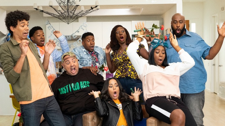 A scene from Astronomy Club on Netflix. The eight cast members, sitting together in an open concept apartment, are reacting shocked and scared to something off camera.