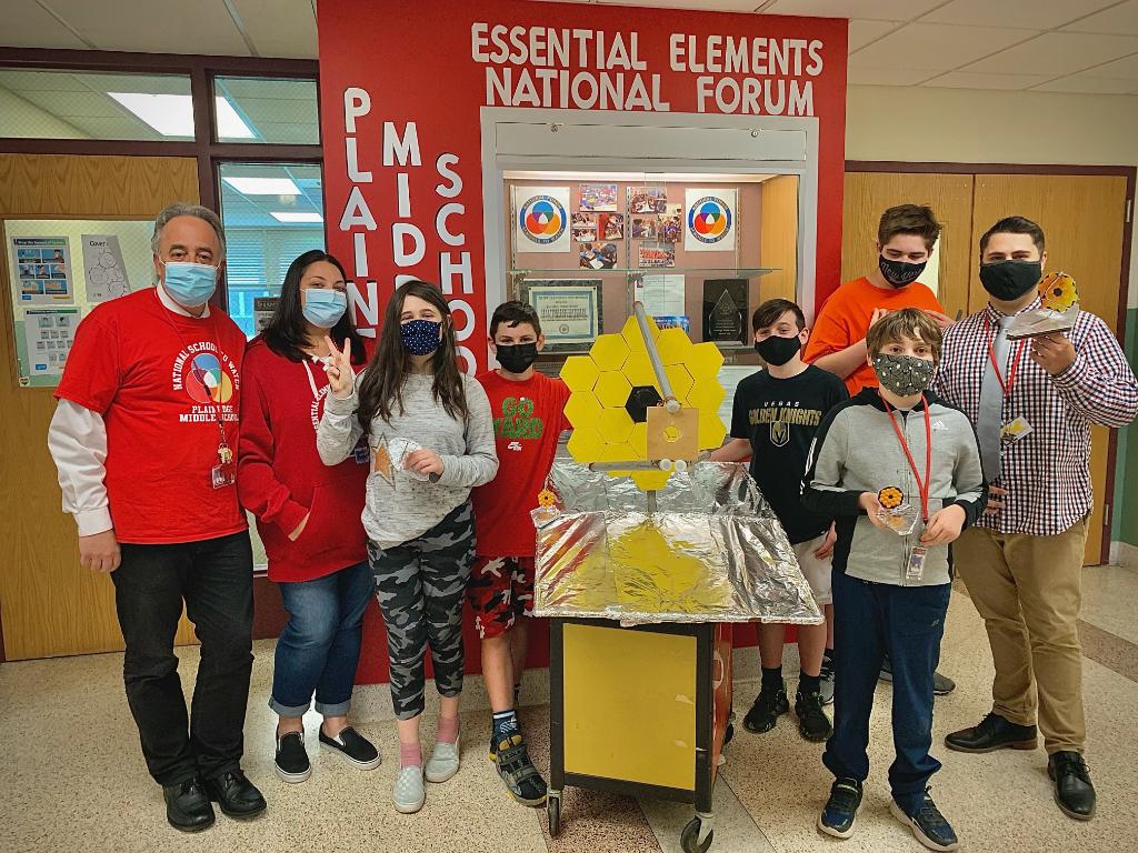 Mr. Caprioli, his students, and the principals of Plainedge Middle School stand with the Webb models created in Mr. Caprioli's classes. A large-scale model is at the center of the picture, while the students hold smaller-scale Webb models.