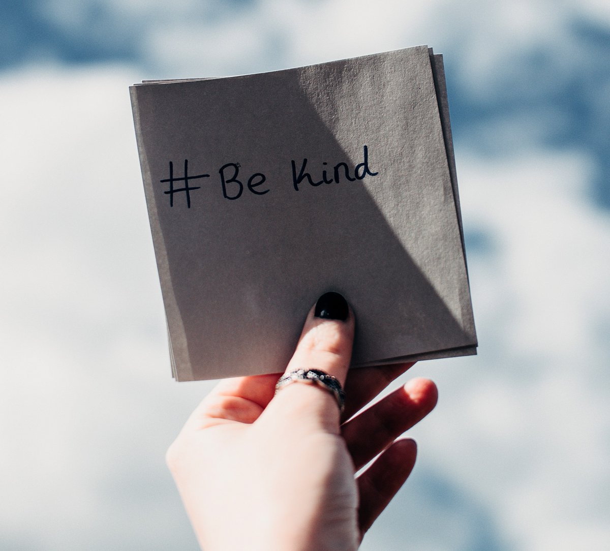 A hand holds a piece of paper that says #Be Kind 