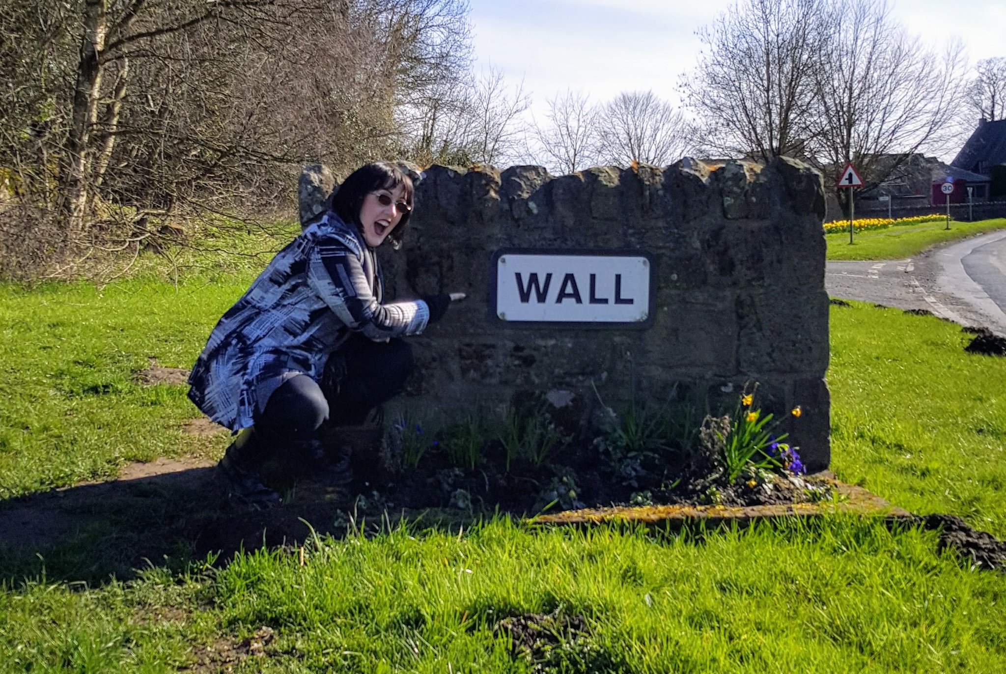 An image of Icy posing next to the village sign for Wall in Northumberland.