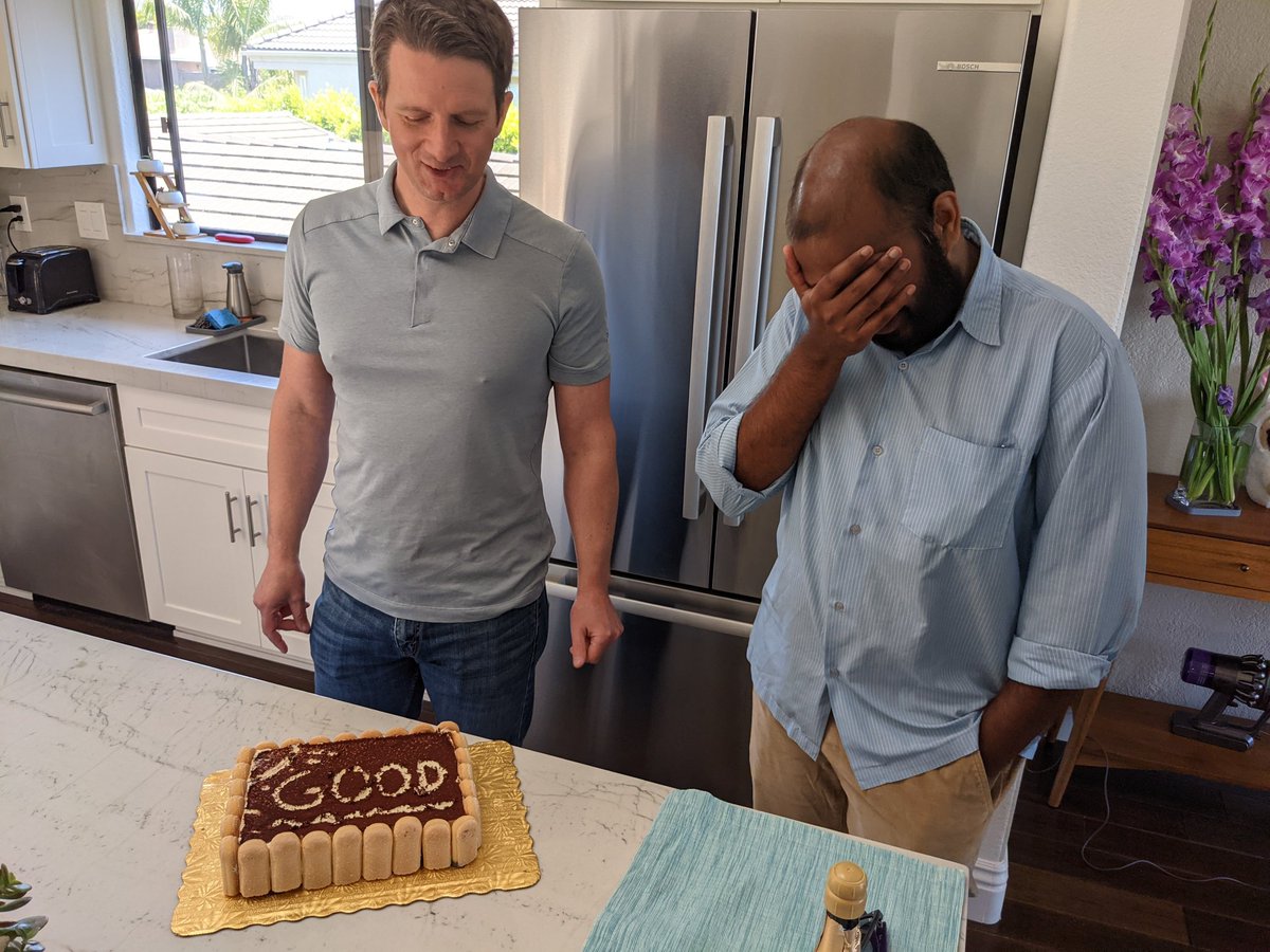 Two people looking at a cake that says "good"