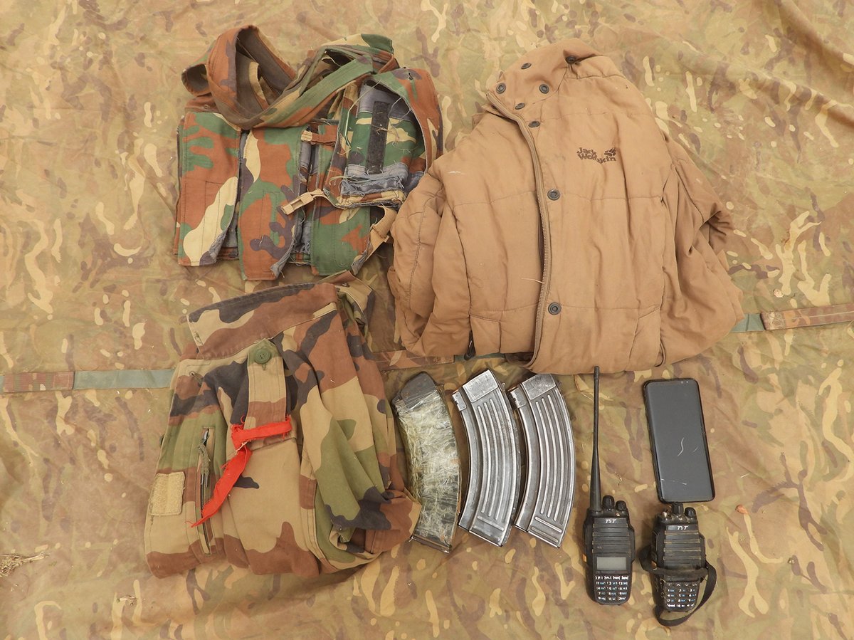Clothing including camouflage jackets, two radios and three AK47 magazines laid out on the ground.