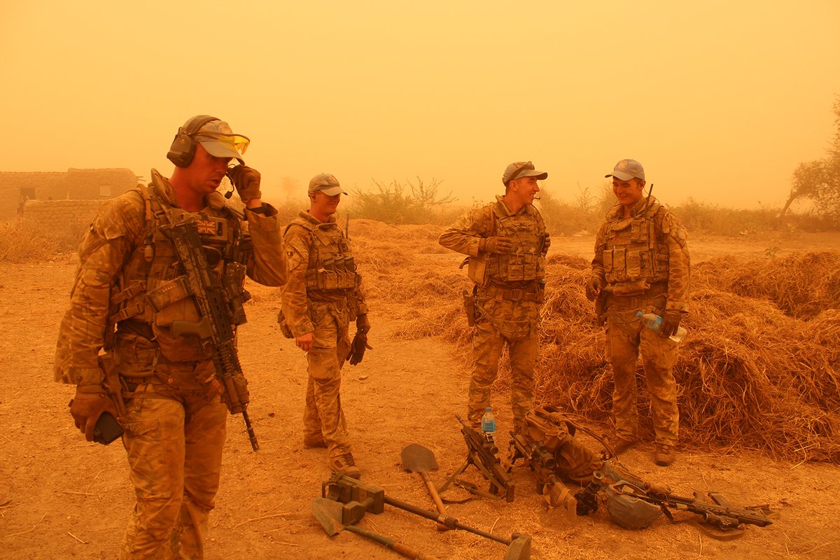 British soldiers stand and speak to each other as they coordinate the search amidst the orange haze of the sandstorm.