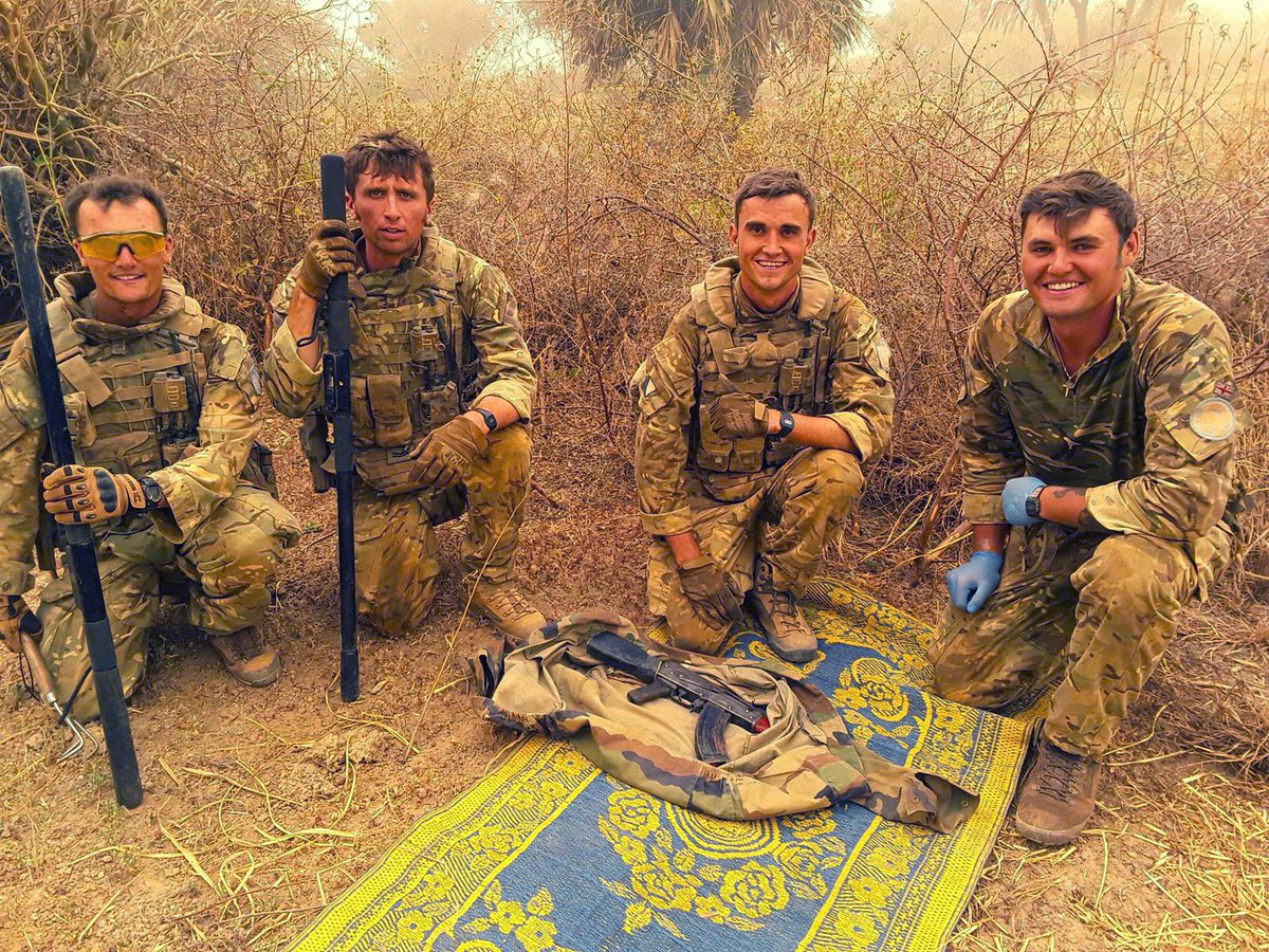 A group of soldiers kneel and smile as they pose next to one of the AK47 rifles they found during the search.