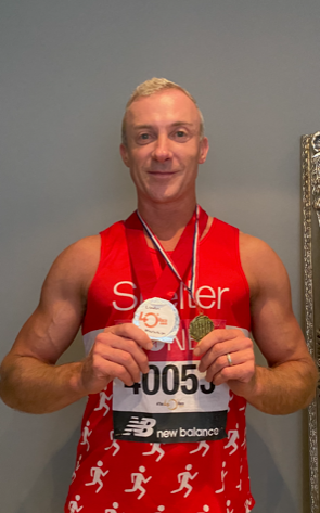 A man in a red Shelter running vest shows off his medals.