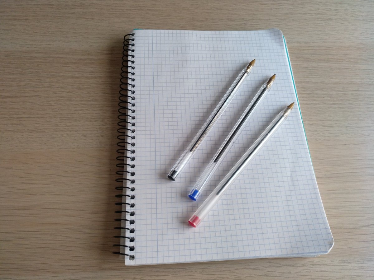 A notebook with three different color pens on top