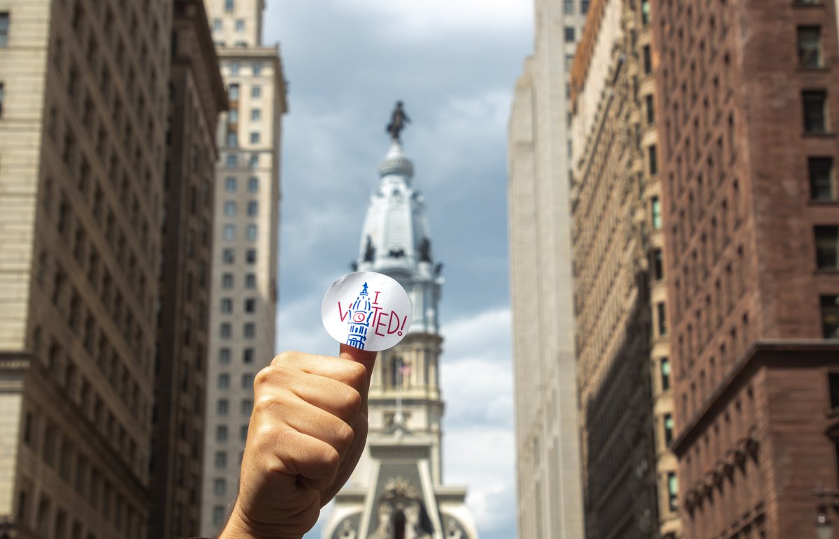 a person with an i voted sticker on their thumb giving the thumbs up in front of city hall