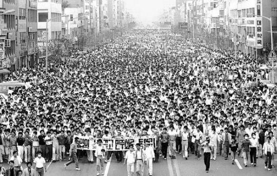 A massive crowd in the hundreds of thousands walking down a wide city avenue for as far as the eye can see