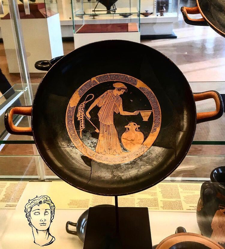 HellenisticHist's tweet photo. The red-figure kylix dated to 490-480 BC from Attica attributes to the Brygos painter, shows a woman who is about to take wine with a long ladle from a jar to fill her skyphos. Behind her hangs a case for an aulos or double flute. #redfigure #kyliw #anciengreece #classics https://t.co/DZsIJ7Tj2D