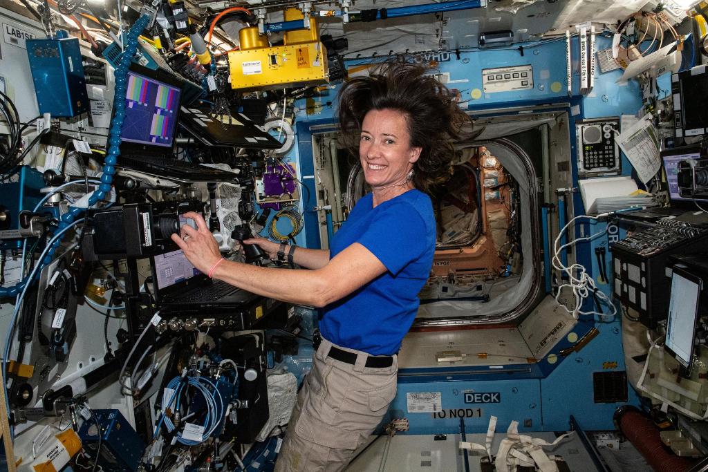 Megan McArthur working aboard the space station, smiling and wearing a blue polo and khakis. 